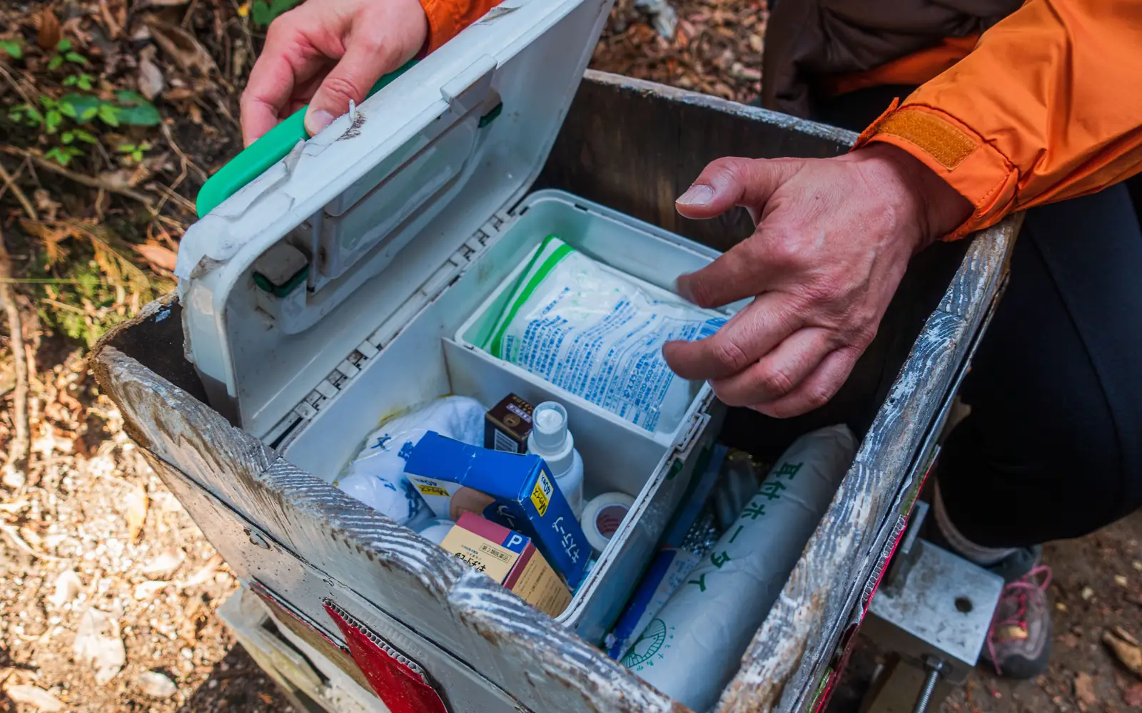 A hiker opens a first-aid kit with supplies arranged for an outdoor day.
