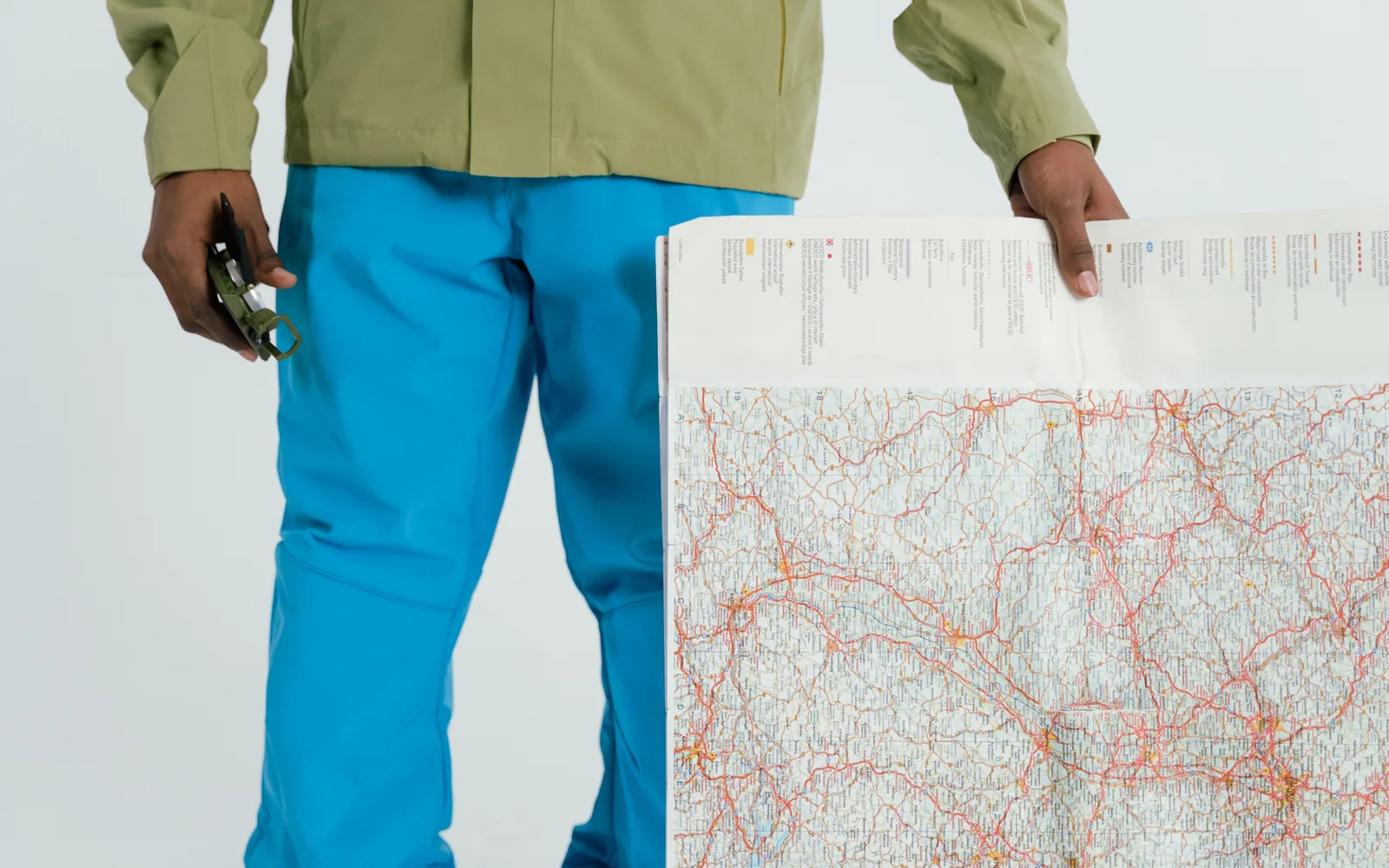 A hiker holds a folded map and compass in an outdoor setting.