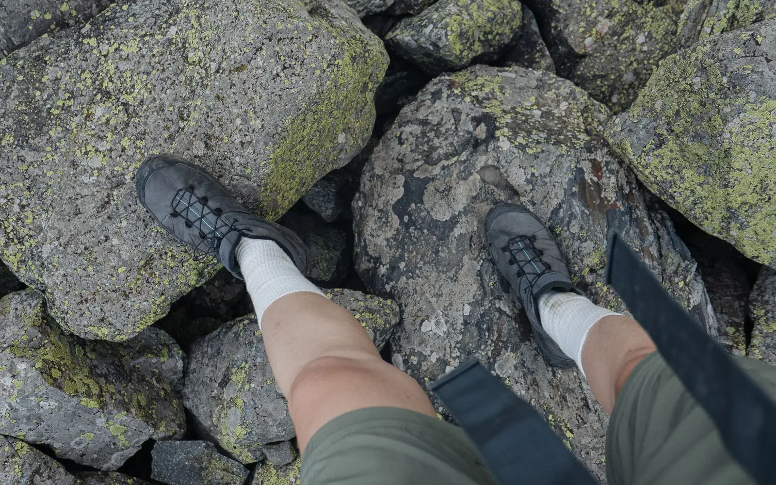 A hiker’s shoes and socks stand on moss-covered rocks in a trail setting.